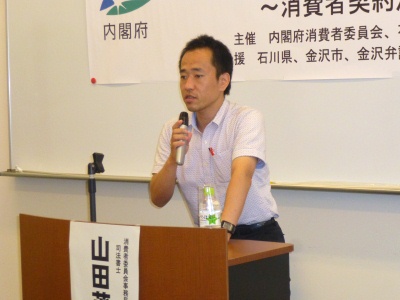 演台に手を置き、話をする山田司法書士の写真