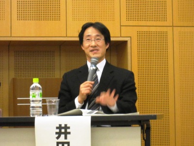 マイクを手にジェスチャーをまじえ話をする井田理事長の写真