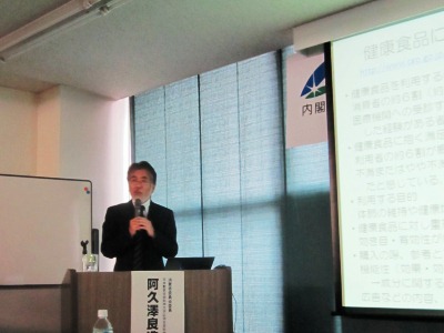 資料を映し出したプロジェクタとその横で話をする阿久澤委員の写真