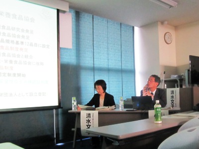 プロジェクタを見上げ話をする日本健康・栄養食品協会の小林氏、その横には資料に目をやる滋賀県消費生活センターの清水氏が写っている写真