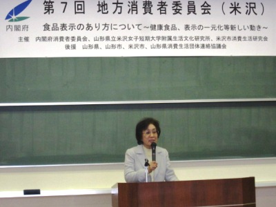 「第７回地方消費者委員会（米沢）」の横断幕を背に挨拶をされる遠藤学長の写真