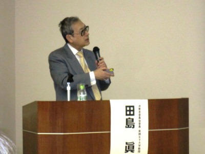 プロジェクタを操作しながらマイクを手に話をする田島委員の写真