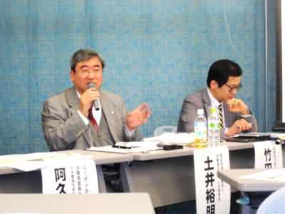 マイクを持ち、話をする消費者ネット・しが理事長の土井氏と、資料を見る消費者庁の竹田食品表示企画課長の写真