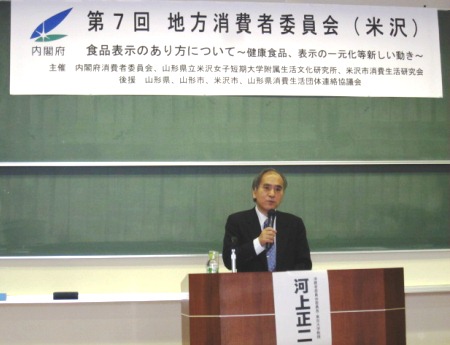 「第７回地方消費者委員会（米沢）」の横断幕を背に講演する河上委員長の写真