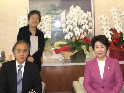 前列に河上委員長と吉村知事が着席し、その後ろに原事務局長が立っている写真。